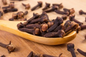 Heap of cloves with wooden spoon on table, seasoning for cooking